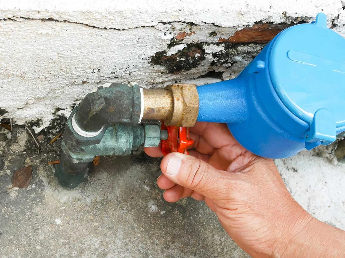 Hand turning the main water shutoff valve in a meter box