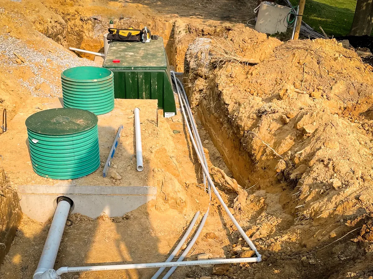 New septic tank and green riser lids set in an open excavation with inlet piping