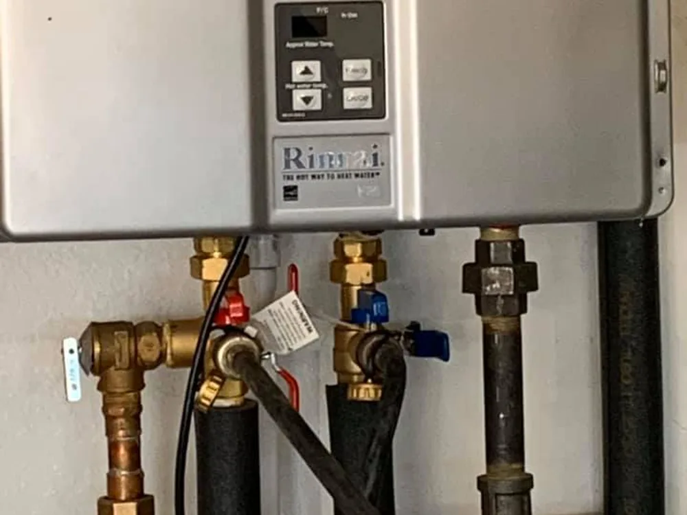 Close-up of the isolation valves and service ports under a wall-mounted tankless water heater