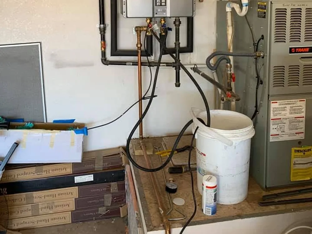 Tankless water heater being flushed, with hoses running down into a bucket