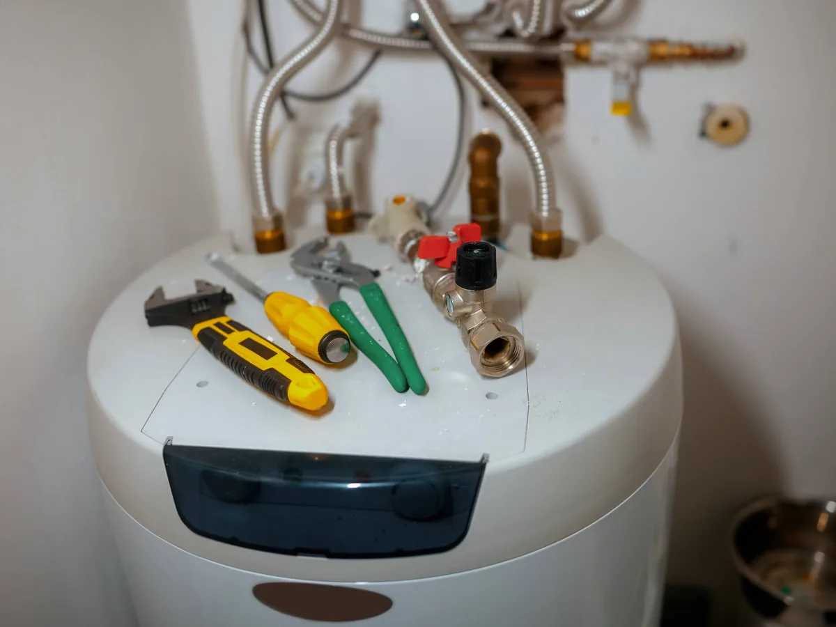 Hand tools laid on top of a tank water heater with its water connections above